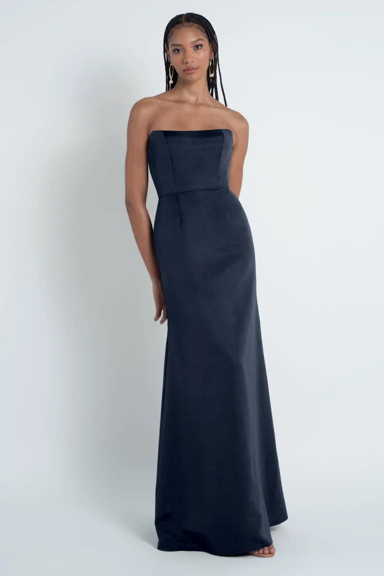 A woman in a strapless Paige - Jenny Yoo Bridesmaid Dress stands against a plain background, perfectly suited for any sophisticated bridal party from Bergamot Bridal.