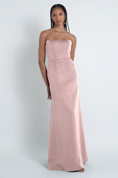 Woman in a pink Jenny Yoo bridesmaid dress from Bergamot Bridal made of Luxe Faille fabric standing against a grey background.