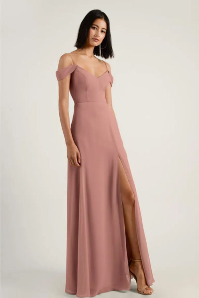 Woman in an elegant blush pink chiffon bridesmaid dress with off-shoulder sleeves and a side slit, the Priya - Bridesmaid Dress by Jenny Yoo from Bergamot Bridal.