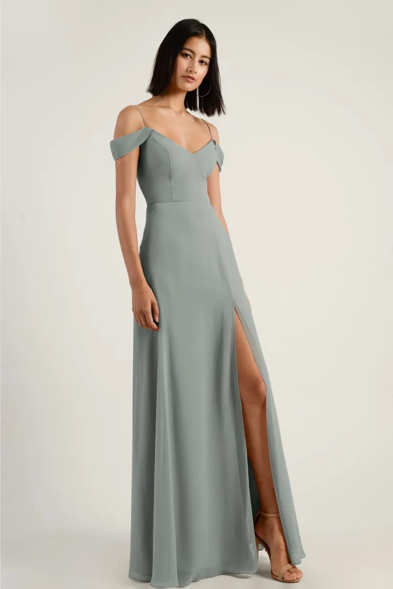 Woman in an elegant grey off-the-shoulder gown with a high slit and A-line skirt, Priya - Bridesmaid Dress by Jenny Yoo at Bergamot Bridal.
