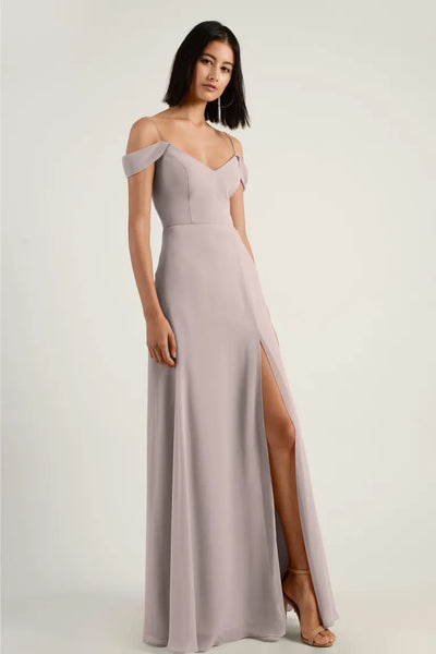 Woman in an elegant chiffon Priya bridesmaid dress by Jenny Yoo with an off-the-shoulder sleeve and a thigh-high slit from Bergamot Bridal.