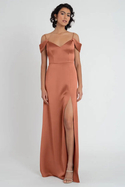 Woman in an elegant Priyanka bridesmaid dress by Jenny Yoo in terracotta satin with off-the-shoulder sleeves and side slit from Bergamot Bridal.