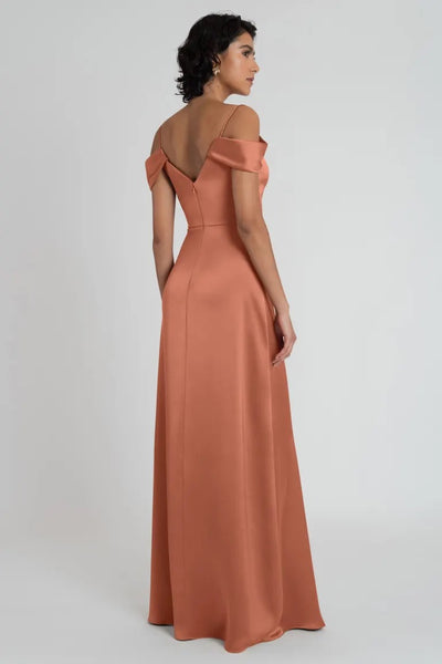 Woman in an elegant off-the-shoulder terracotta V-neck Priyanka - Bridesmaid Dress by Jenny Yoo evening gown viewed from the side from Bergamot Bridal.