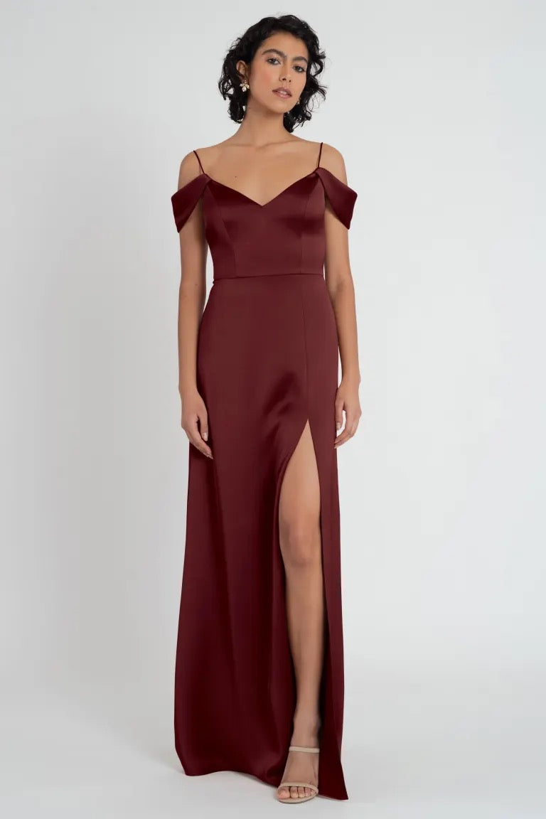 Woman posing in an elegant off the shoulder burgundy evening gown with a side slit - Priyanka Bridesmaid Dress by Jenny Yoo from Bergamot Bridal.