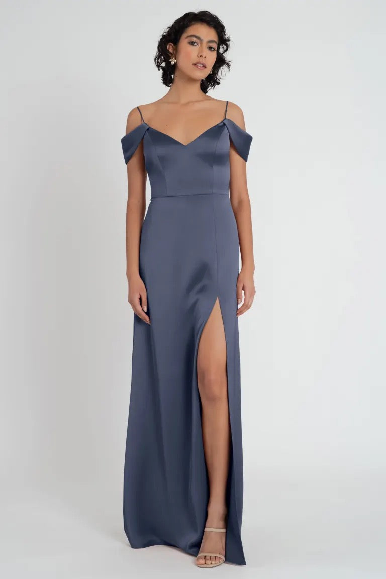 Woman in an elegant grey evening gown with a thigh-high slit and off-the-shoulder sleeves, wearing the Priyanka - Bridesmaid Dress by Jenny Yoo from Bergamot Bridal.