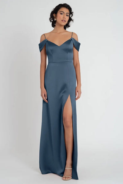 A woman models a Priyanka - Bridesmaid Dress by Jenny Yoo, in collaboration with Bergamot Bridal, with an off-the-shoulder sleeve and thigh-high slit.