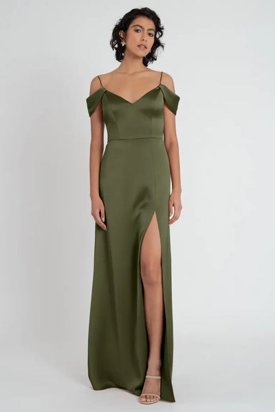 A woman wearing an olive green satin Priyanka bridesmaid dress by Jenny Yoo with a thigh-high slit and off-the-shoulder sleeves from Bergamot Bridal.