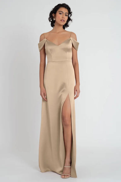 Woman posing in an elegant satin Priyanka bridesmaid dress by Jenny Yoo with a thigh-high slit and off-the-shoulder sleeves from Bergamot Bridal.