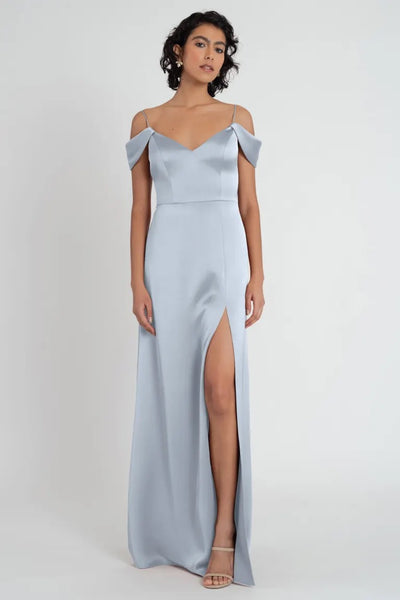 A woman in an elegant blue satin V-neck Priyanka bridesmaid dress by Jenny Yoo with a thigh-high slit and off the shoulder sleeve from Bergamot Bridal.