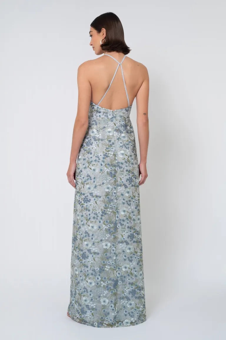 A woman is seen from the back, wearing a long floral Jenny Yoo Bridesmaid Dress with an Ophelia embroidery halter neckline and crisscross straps from Bergamot Bridal.