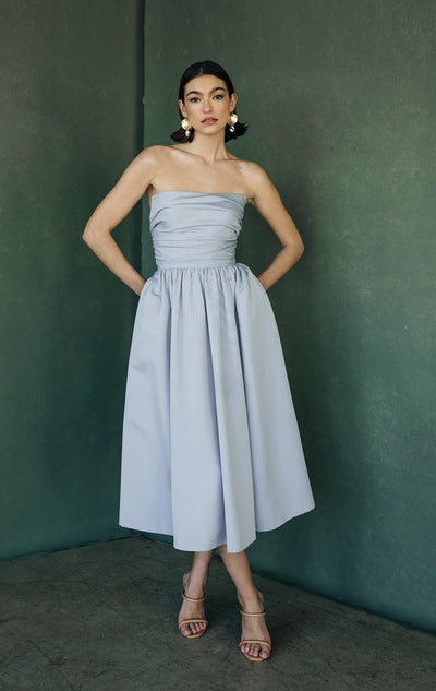 A woman wearing a strapless Jenny Yoo Bridesmaid Dress and high-heeled sandals stands against a green wall from Bergamot Bridal.