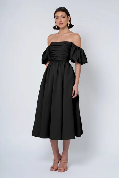 Woman posing in an off-the-shoulder black midi Jenny Yoo Bridesmaid Dress with detachable puff sleeves and heeled sandals from Bergamot Bridal.