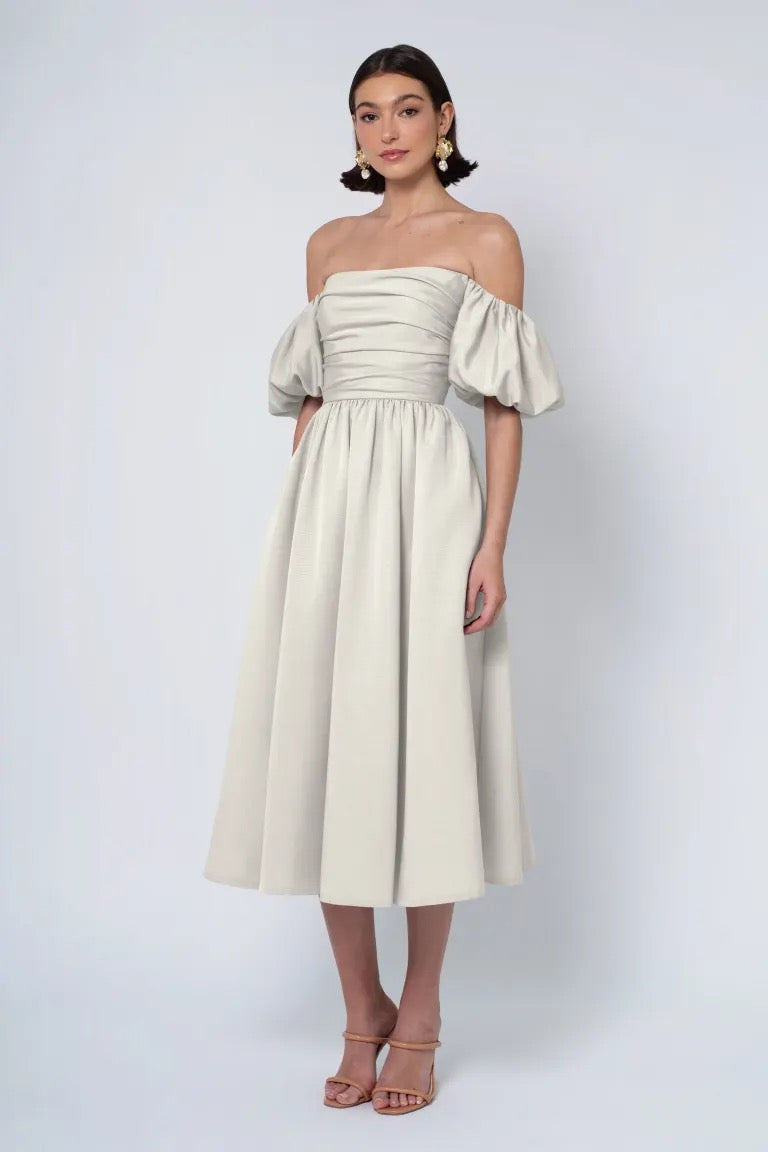 Woman modeling a Jenny Yoo Bridesmaid Dress from Bergamot Bridal featuring a strapless neckline, ivory midi length with puff sleeves, and paired with heeled sandals.