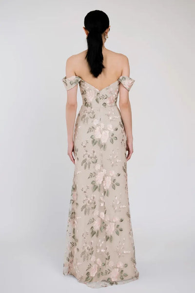 A woman with a ponytail wears the Reina dress by Bergamot Bridal, an off-the-shoulder floral gown featuring exquisite Ophelia embroidery. She is viewed from the back, showcasing the elegant design and sweetheart neckline of this Jenny Yoo bridesmaid dress.