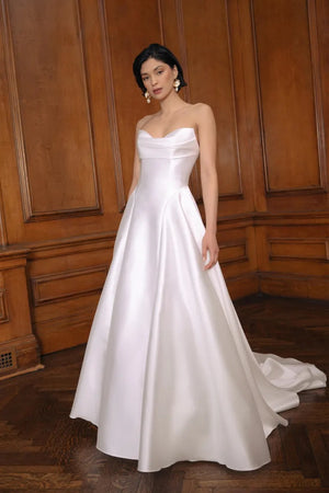 Woman in an elegant white off-shoulder Jenny Yoo Wedding Dress featuring a drop waist silhouette, standing in a wood-paneled room from Bergamot Bridal.