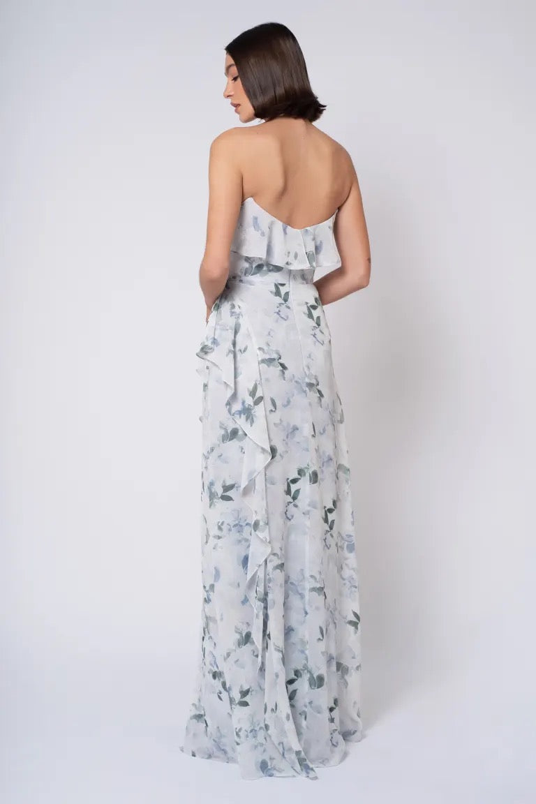 A woman in an elegant floral printed chiffon Salma Print - Jenny Yoo Bridesmaid Dress viewed from the back, featuring an off-the-shoulder neckline by Bergamot Bridal.