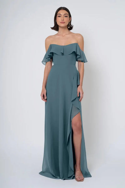 Woman posing in an elegant Salma - Jenny Yoo Bridesmaid Dress with an off-the-shoulder neckline and a high side slit from Bergamot Bridal.