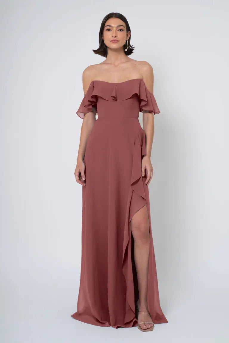 Woman in an elegant off-the-shoulder terracotta Salma - Jenny Yoo Bridesmaid Dress chiffon dress with a side slit from Bergamot Bridal.