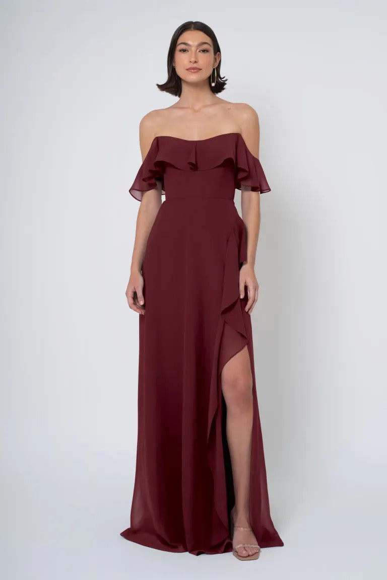 Woman in an elegant burgundy Salma - Jenny Yoo Bridesmaid Dress with a ruffled neckline and a side slit from Bergamot Bridal.