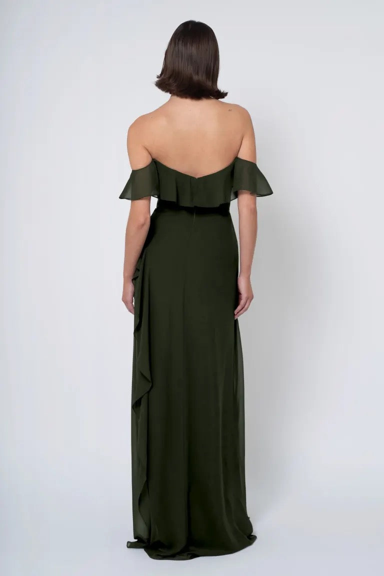 Woman posing in a long green Salma - Jenny Yoo Bridesmaid Dress with a ruffle detail, viewed from the back, from Bergamot Bridal.