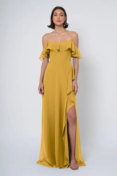 Woman in a mustard Jenny Yoo Bridesmaid Dress with off-the-shoulder neckline, ruffle detail, and a side slit from Bergamot Bridal.