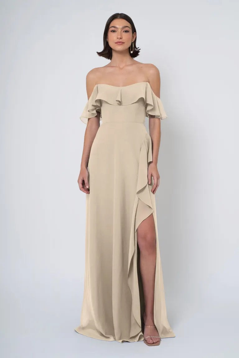 Woman in an elegant beige Jenny Yoo Bridesmaid dress featuring an off-the-shoulder neckline and a side slit from Bergamot Bridal.