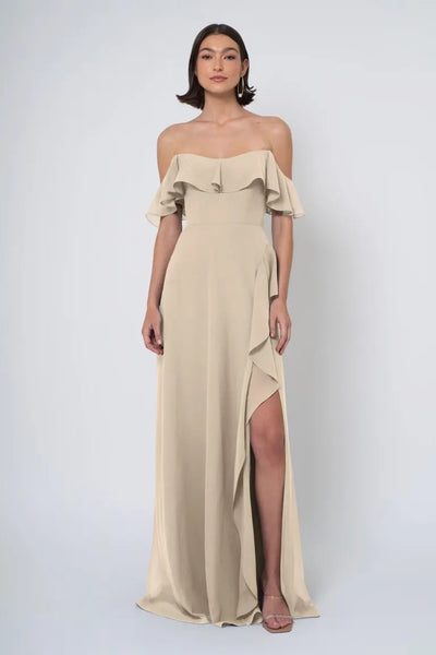 Woman in an elegant beige Jenny Yoo Bridesmaid dress featuring an off-the-shoulder neckline and a side slit from Bergamot Bridal.