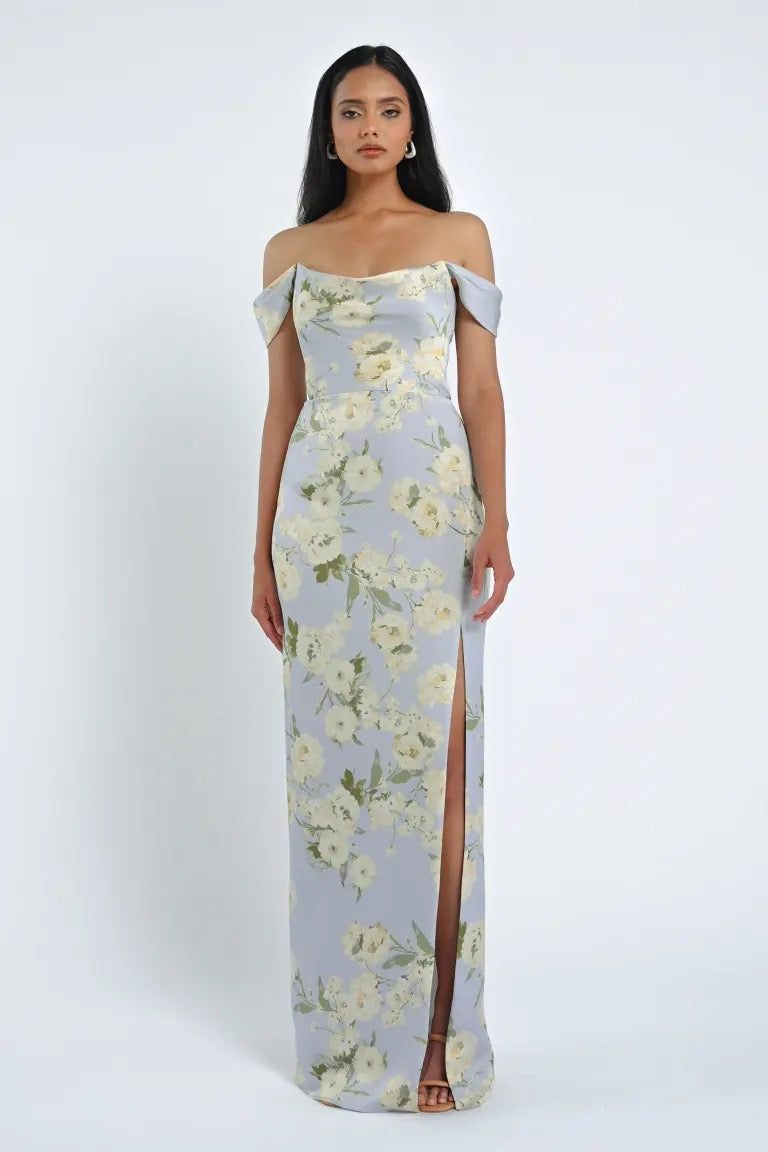 A woman stands in a strapless, off-the-shoulder, Sawyer Verona Print Bridesmaid Dress by Jenny Yoo, featuring a thigh-high slit, posing against a plain white background. The dress is showcased under the Bergamot Bridal brand.