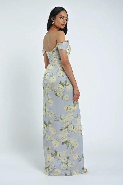 A woman in a light blue Sawyer Verona Print Bridesmaid Dress by Jenny Yoo, available from Bergamot Bridal, featuring off-the-shoulder sleeves, stands facing sideways against a plain white background.