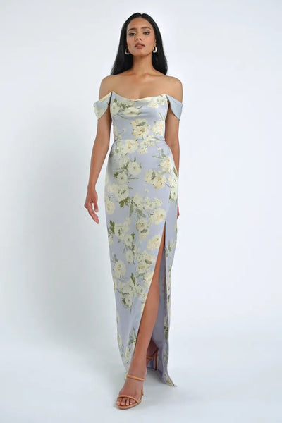 A woman wearing the Sawyer Verona Print Bridesmaid Dress by Bergamot Bridal, designed by Jenny Yoo, featuring off-the-shoulder sleeves and a thigh-high slit, paired with nude heels, stands against a plain white background.