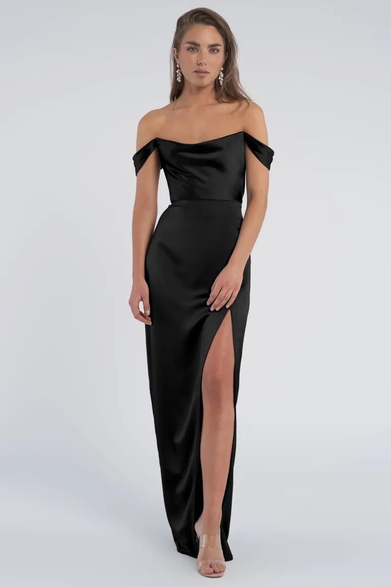 Woman posing in an elegant off-the-shoulder Sawyer Bridesmaid Dress by Jenny Yoo with a slim skirt and a thigh-high slit from Bergamot Bridal.