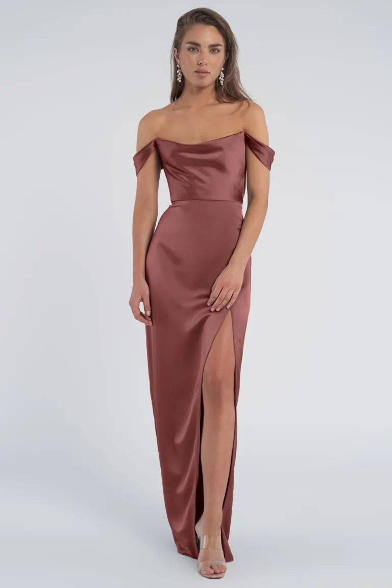 A woman modeling a luxe satin Sawyer - Bridesmaid Dress by Jenny Yoo with off the shoulder sleeves and a thigh-high slit from Bergamot Bridal.