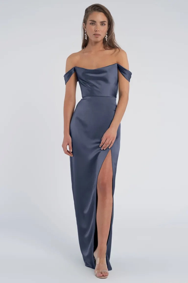 Woman in a Sawyer - Bridesmaid Dress by Jenny Yoo, from Bergamot Bridal, in luxe satin, off-the-shoulder slate blue evening gown with a thigh-high slit.