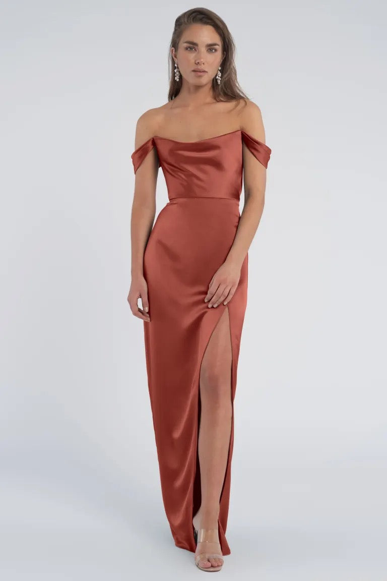 Woman posing in a sleek off-the-shoulder sleeves satin dress with a thigh-high slit, the Sawyer - Bridesmaid Dress by Jenny Yoo from Bergamot Bridal.