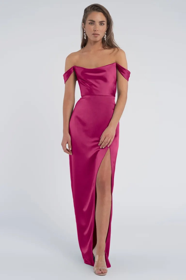 Woman in a luxe satin off-the-shoulder magenta Sawyer - Bridesmaid Dress by Jenny Yoo gown with a thigh-high slit from Bergamot Bridal.