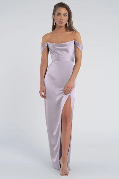 Woman posing in an elegant luxe satin dress with off-the-shoulder sleeves and a thigh-high slit, the Sawyer bridesmaid dress by Jenny Yoo from Bergamot Bridal.