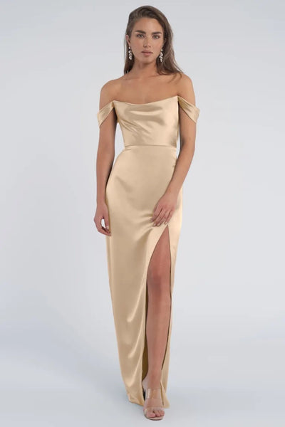 A woman wearing an elegant Sawyer - Bridesmaid Dress by Jenny Yoo with off-the-shoulder sleeves and a thigh-high slit from Bergamot Bridal.