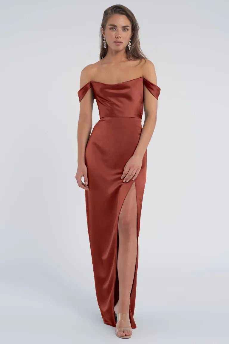 A woman modeling the luxe satin Sawyer bridesmaid dress by Jenny Yoo with off-the-shoulder sleeves and a thigh-high slit from Bergamot Bridal.