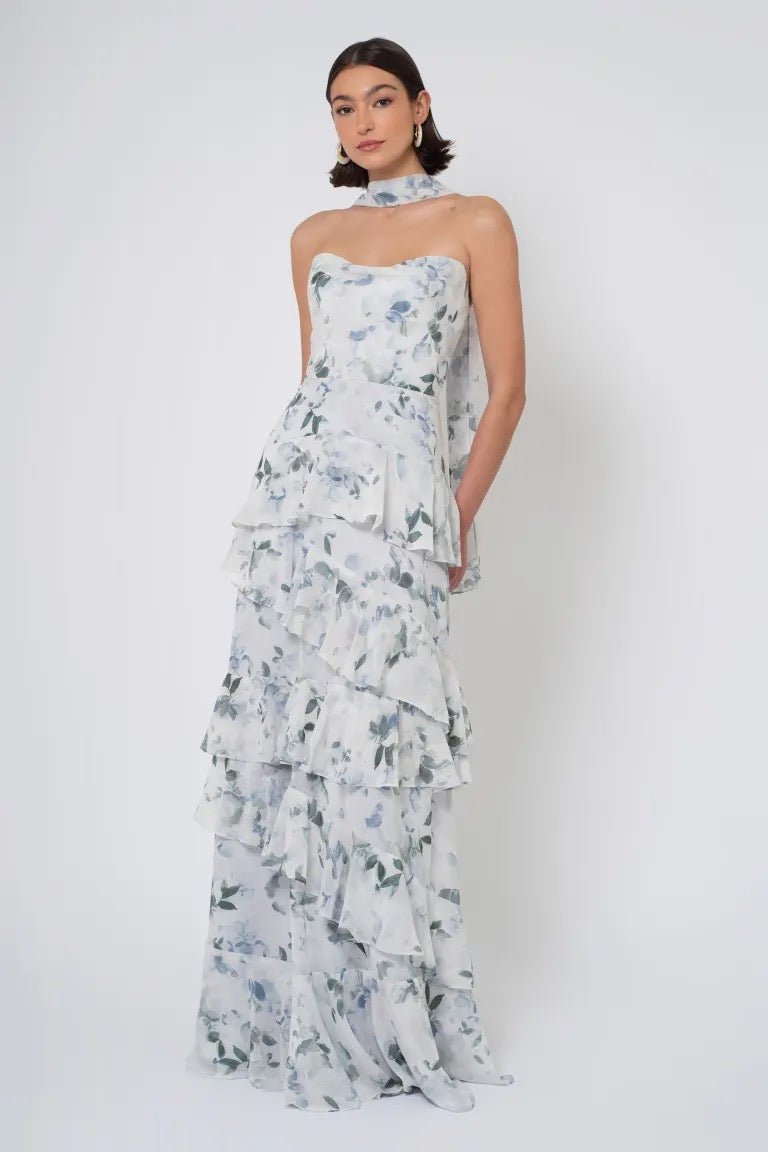 A woman wearing a strapless cowl neckline Simona Print - Jenny Yoo bridesmaid dress with a blue floral print against a plain background from Bergamot Bridal.