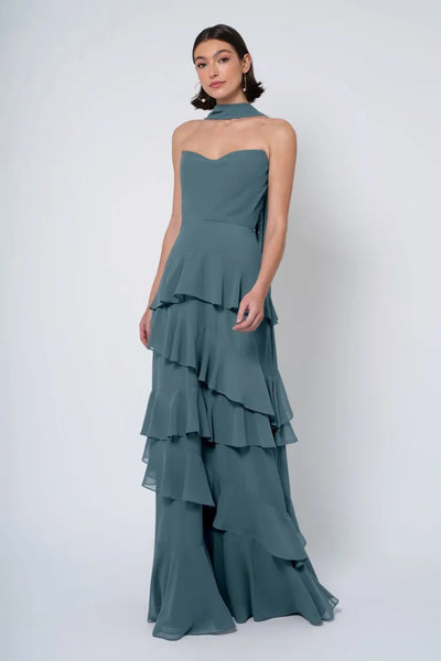 A woman in an elegant strapless cowl neckline Simona - Jenny Yoo Bridesmaid Dress gown with a ruffled skirt, posing against a plain background by Bergamot Bridal.