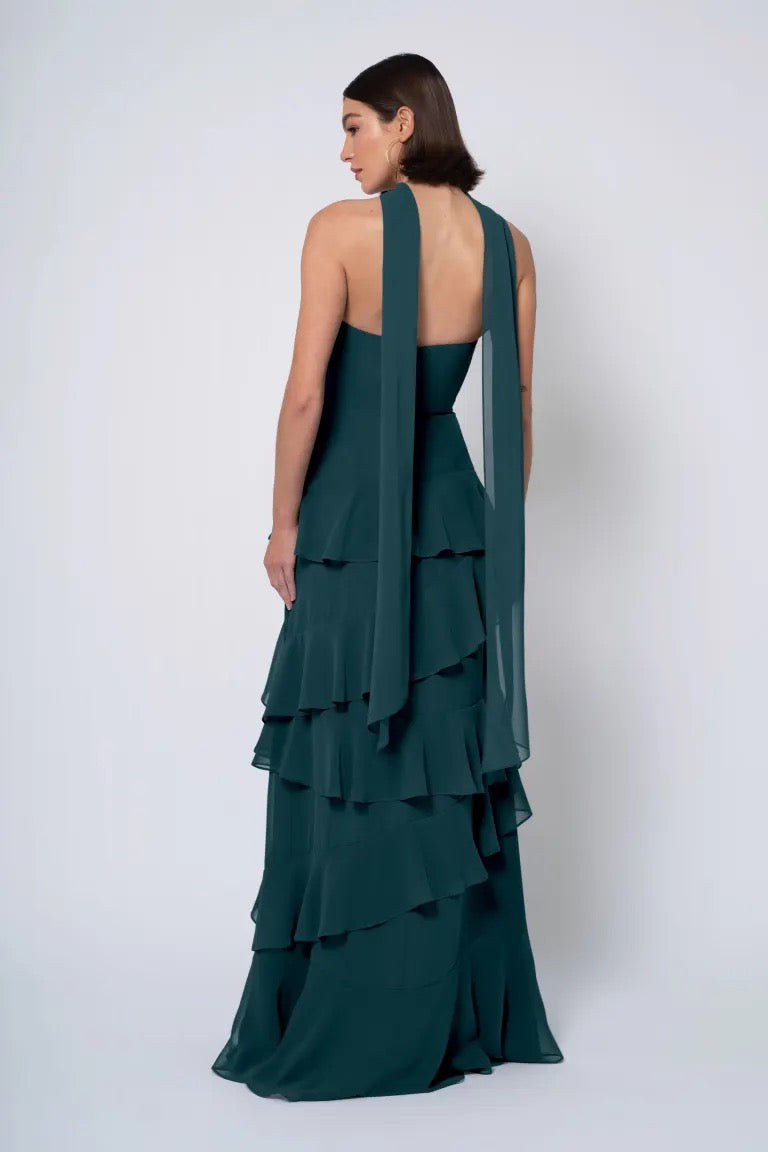 Woman in an elegant green tiered gown with a strapless cowl neckline, posing from the back, wearing the Simona by Jenny Yoo bridesmaid dress from Bergamot Bridal.