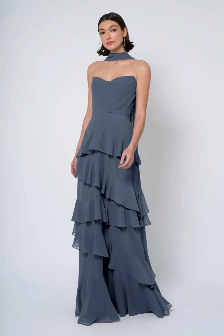 A woman in an elegant strapless cowl neckline gray tiered gown from Bergamot Bridal posing against a white background.