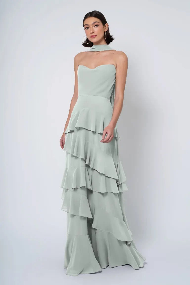 A woman wearing an elegant Jenny Yoo Simona chiffon bridesmaid dress with a strapless cowl neckline in a pastel shade against a white background from Bergamot Bridal.