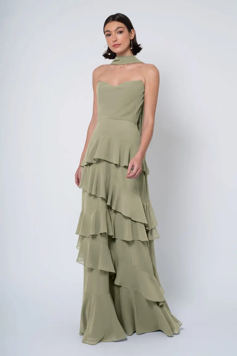 Woman posing in an elegant Simona - Jenny Yoo Bridesmaid Dress from Bergamot Bridal, featuring an olive green strapless cowl neckline tiered gown.