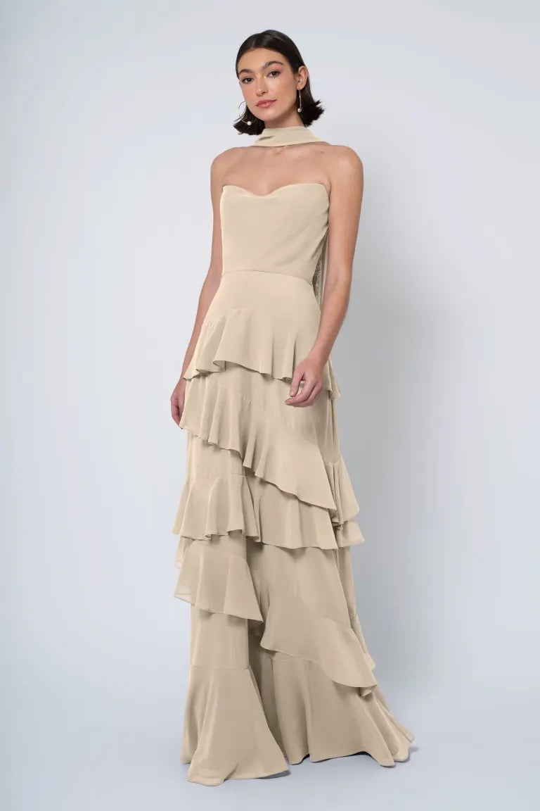 A woman posing in an elegant, strapless cowl neckline gown with a neutral palette and a ruffled skirt, the Simona bridesmaid dress from Jenny Yoo at Bergamot Bridal.