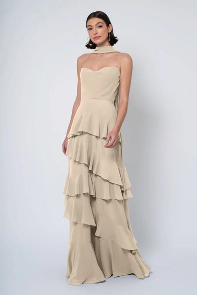 A woman posing in an elegant, strapless cowl neckline gown with a neutral palette and a ruffled skirt, the Simona bridesmaid dress from Jenny Yoo at Bergamot Bridal.