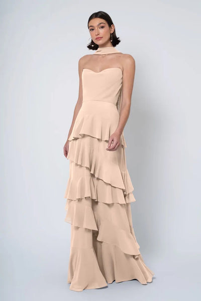 A woman posing in an elegant Simona - Jenny Yoo Bridesmaid Dress with a ruffled skirt against a plain background from Bergamot Bridal.