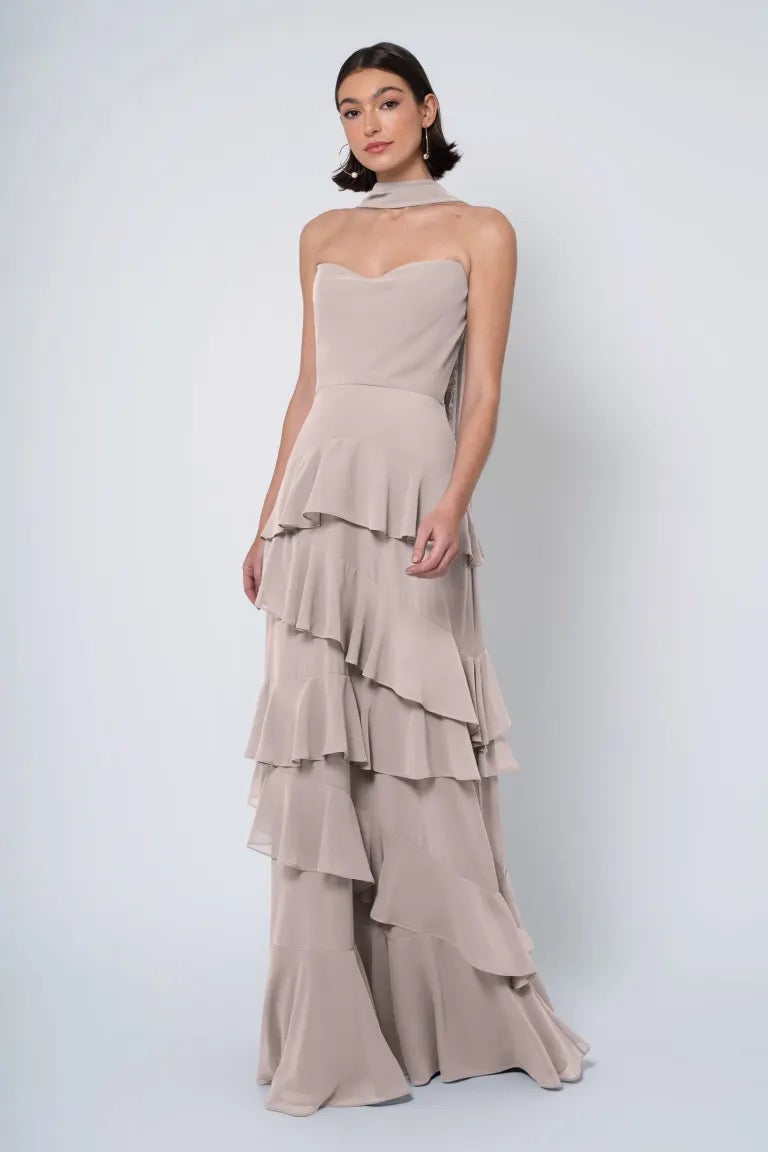 Woman in a tiered strapless Simona - Jenny Yoo Bridesmaid Dress with a ruffled skirt posing against a plain backdrop. (Brand name: Bergamot Bridal)