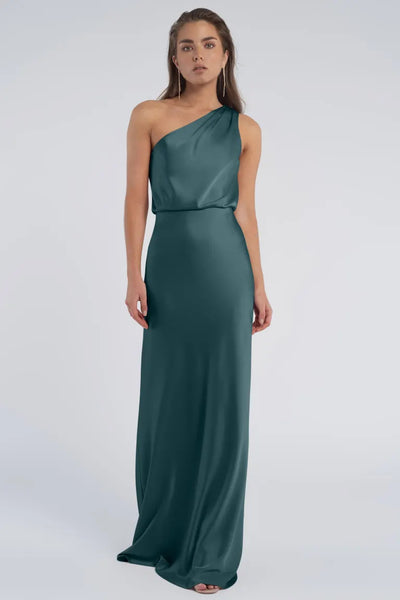 Woman in a one-shoulder luxe satin teal evening gown with a blouson waist standing against a gray background, Sterling by Jenny Yoo Bridesmaid from Bergamot Bridal.
