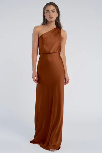 Woman posing in a long, brown, luxurious satin dress with a one-shoulder neckline against a neutral background from Bergamot Bridal's Sterling - Jenny Yoo Bridesmaid collection.